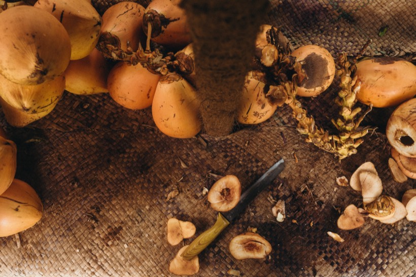 King coconuts on a woven mat seen from above, with a knife and the cut tops lying beside them