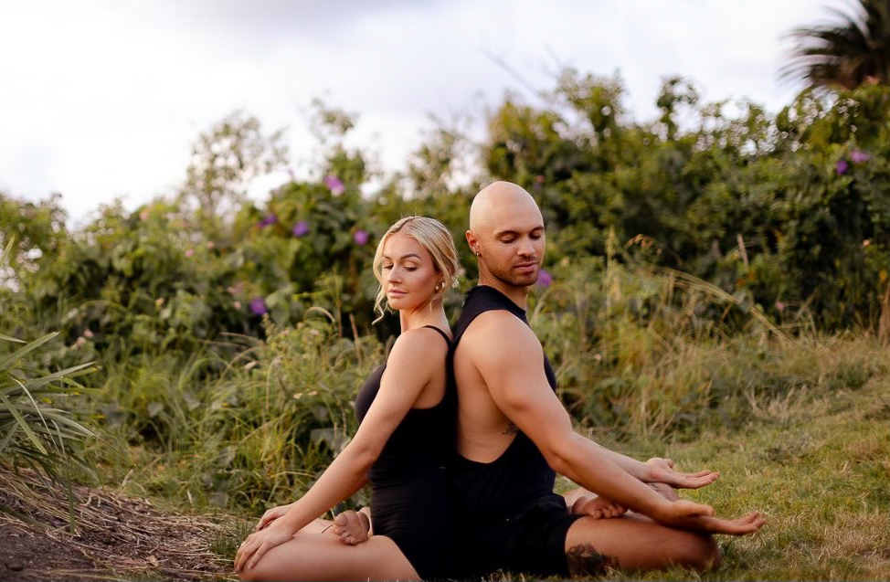  two yoga instructors sitting back to back in mediation position with jungle in the background